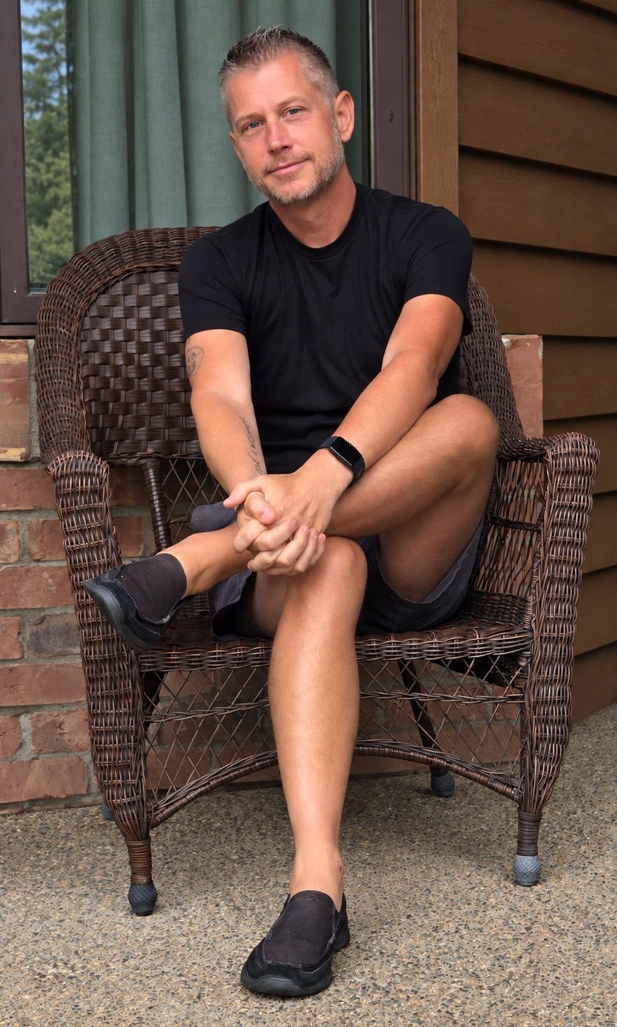 Paul McLellan seated in a wicker chair on a porch in a black T-shirt