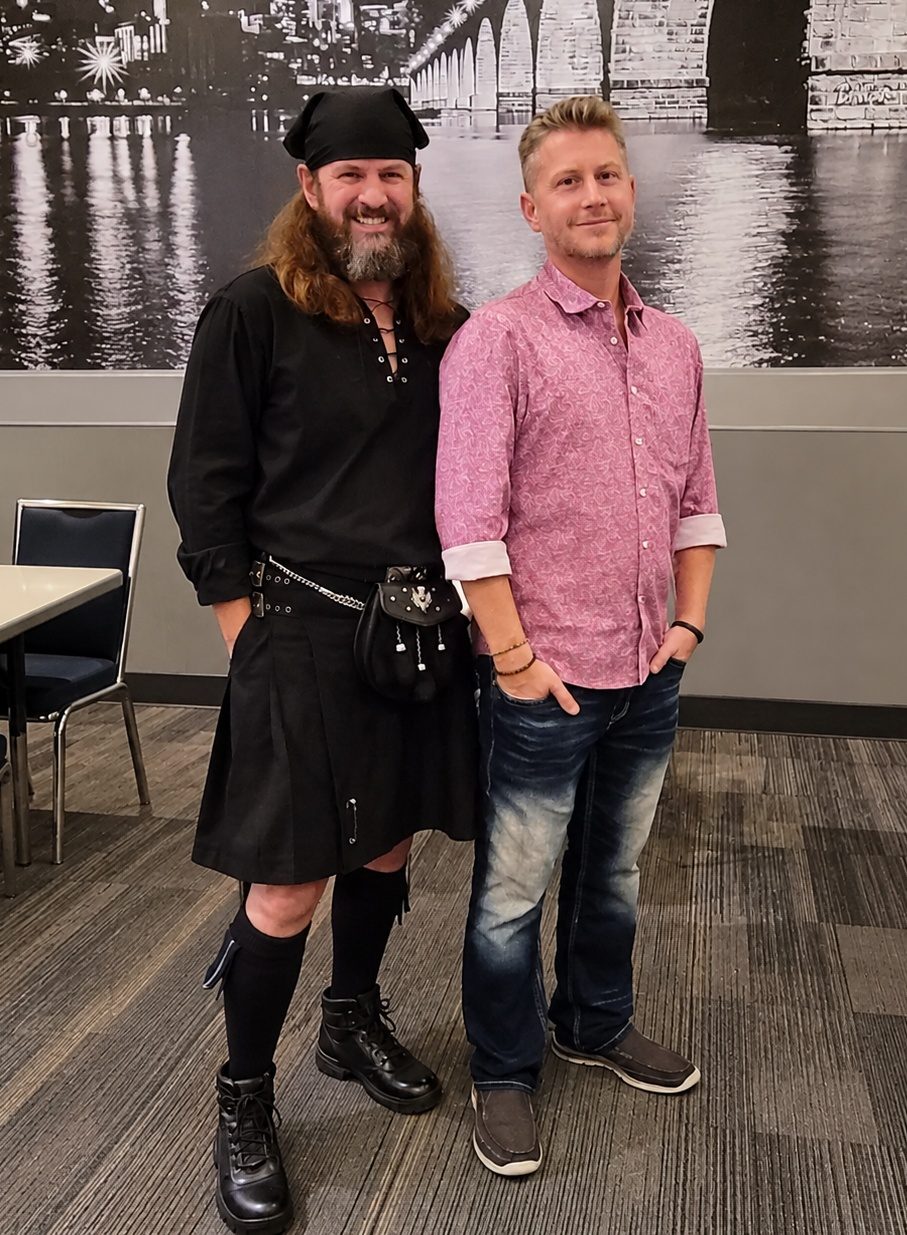 Steve McLellan in a kilt standing beside Paul McLellan in front of a Minneapolis skyline mural