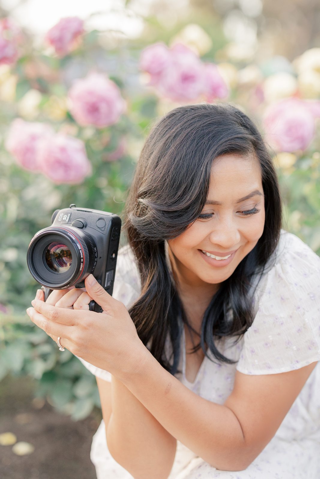 Sarom Thompson smiling as she raises her camera among pink roses