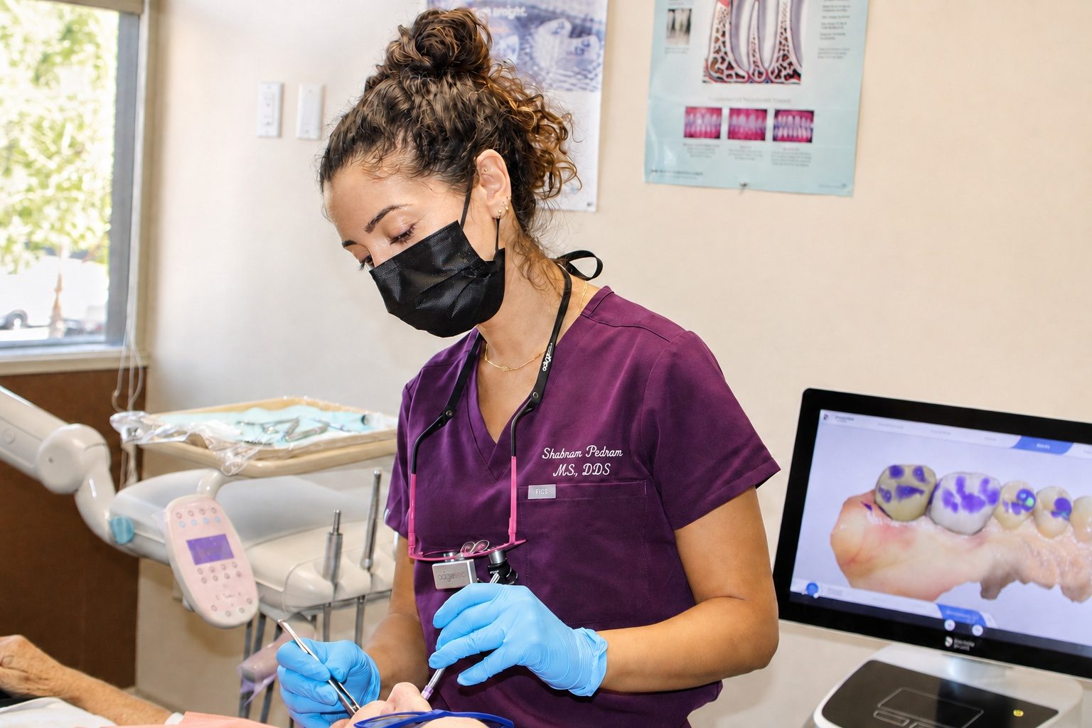 Dr. Shabnam Pedram Scott in purple scrubs and a mask treating a patient at Gentle Dentistry of Poway, with a 3D scan of teeth on the screen behind her