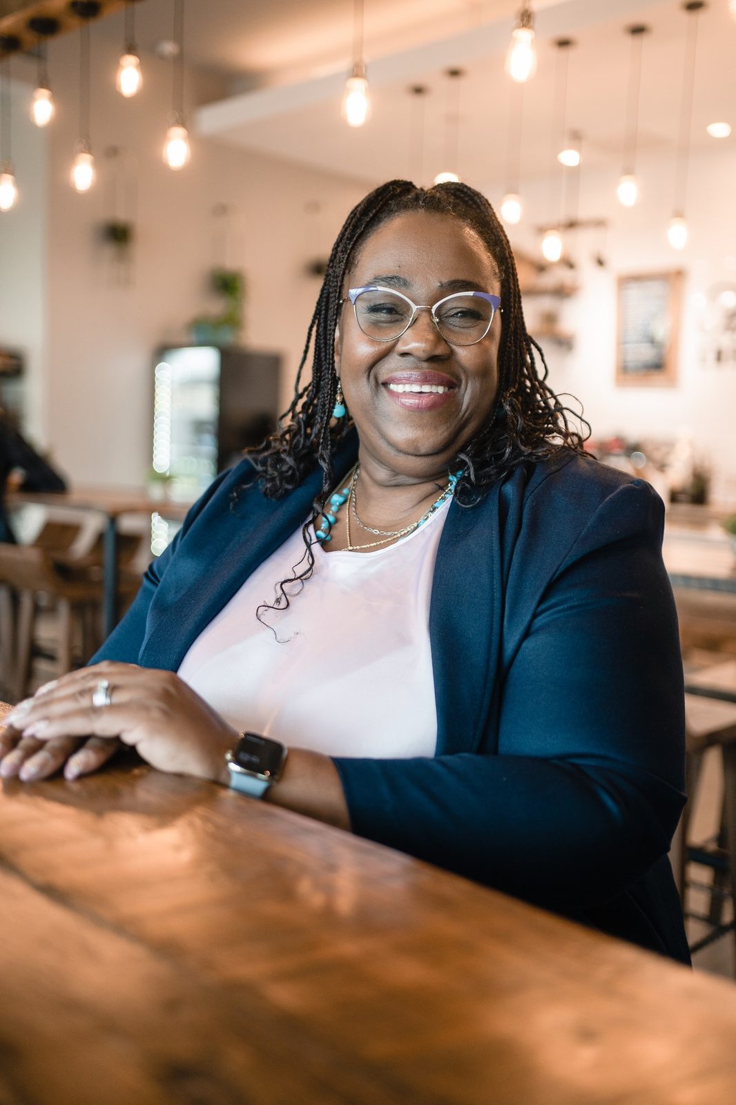 Dr. Sharon M. Jones, founder of My 3 Tiers Emotional Clarity, smiling in glasses and a navy blazer at a wooden table in a cafe