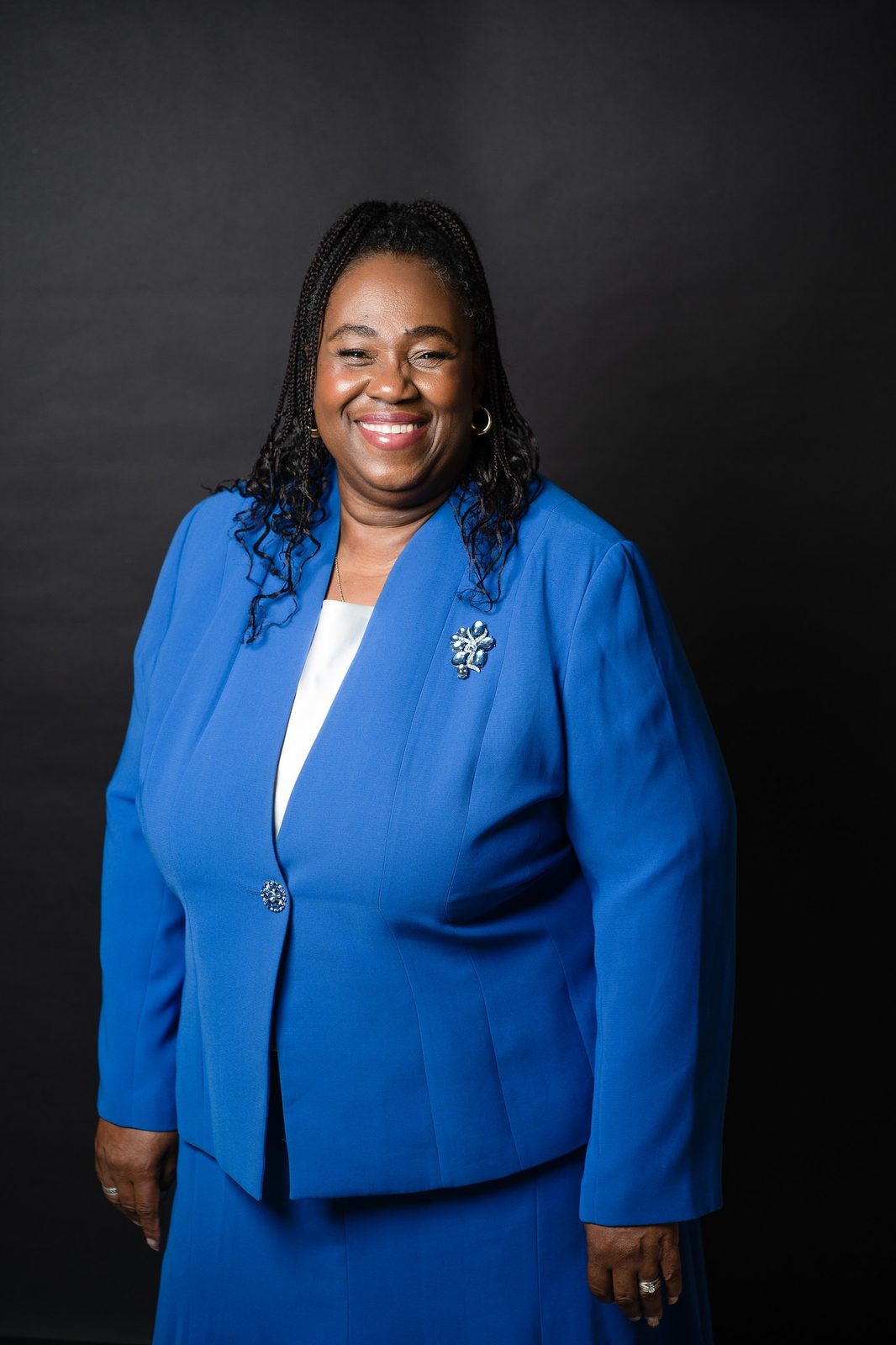 Dr. Sharon M. Jones in a royal blue skirt suit with a silver brooch, smiling against a black studio backdrop