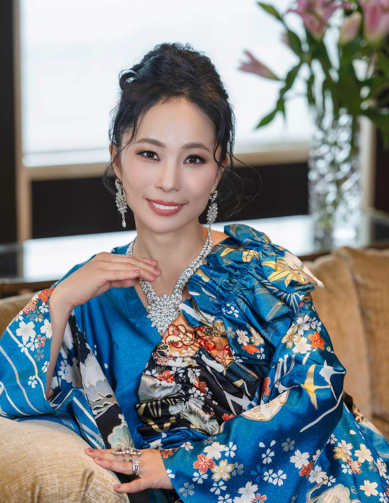 Shiho Brenner, author, kimono ambassador and founder of Kimono Suishin in San Diego, seated in a blue floral kimono with a crystal necklace and earrings