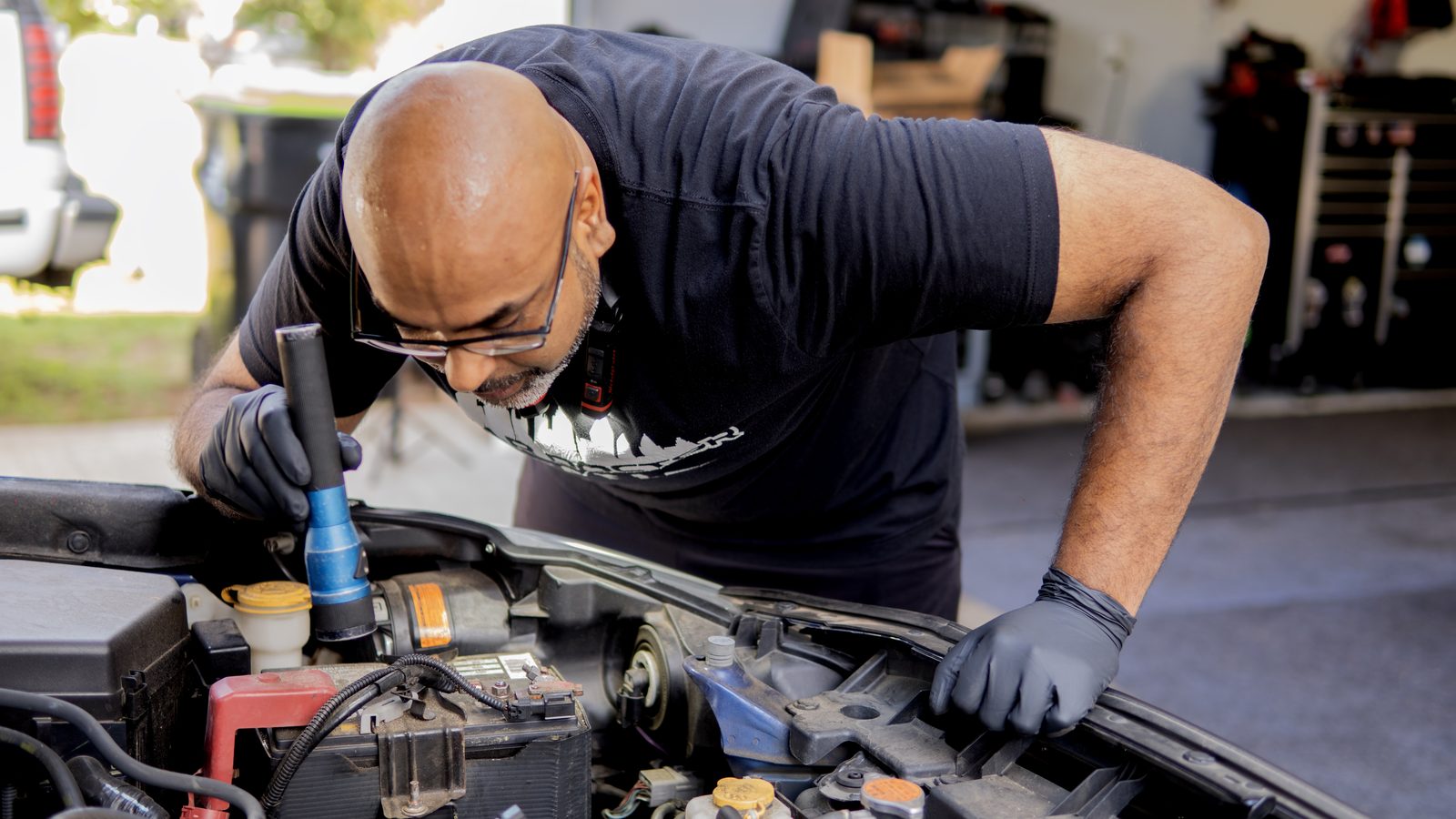 Sri Gadde leaning over an open engine bay with a flashlight