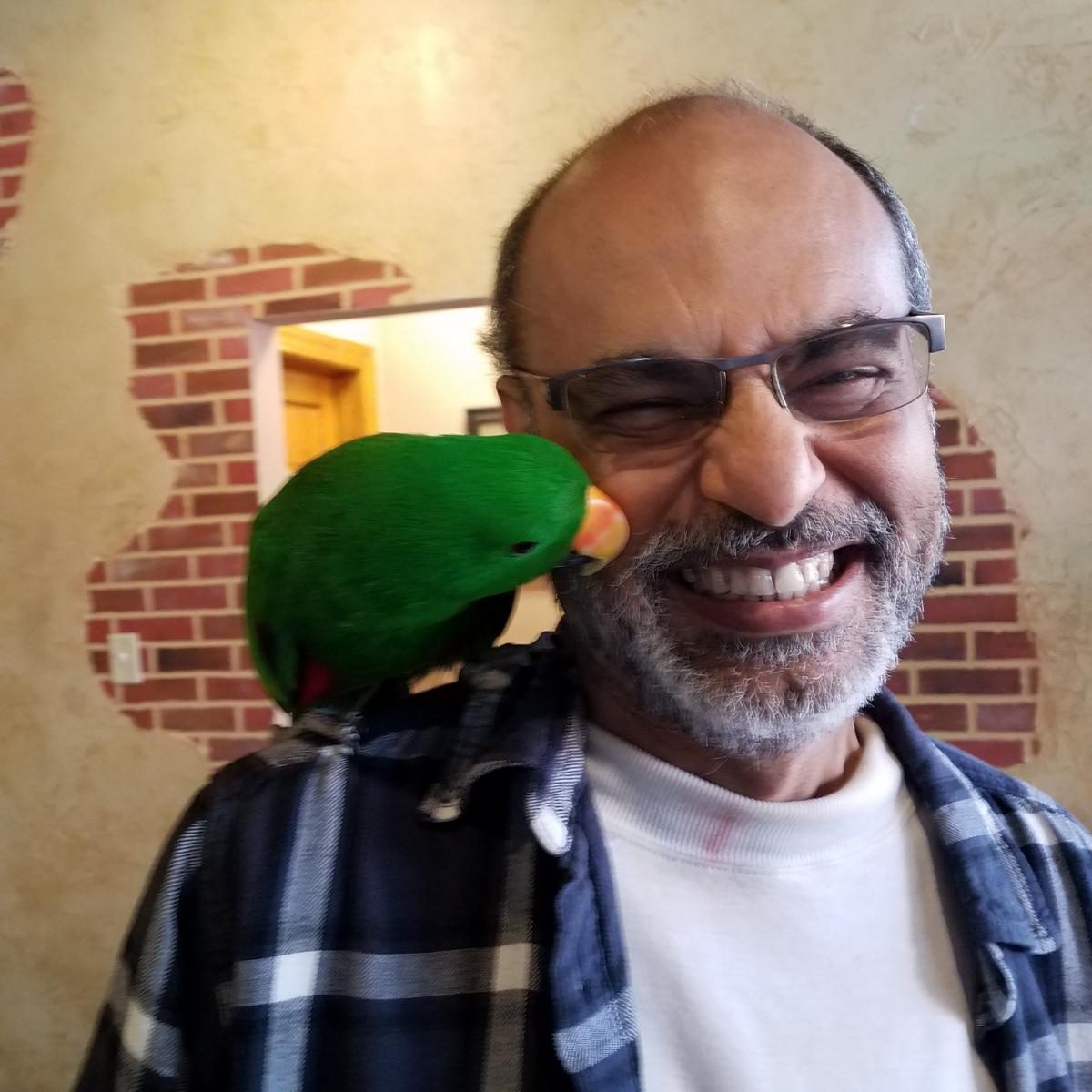 Sridhar Rangaswamy, founder of Dr. JustKidding, Inc. in Orlando, laughing with a green parrot perched on his shoulder