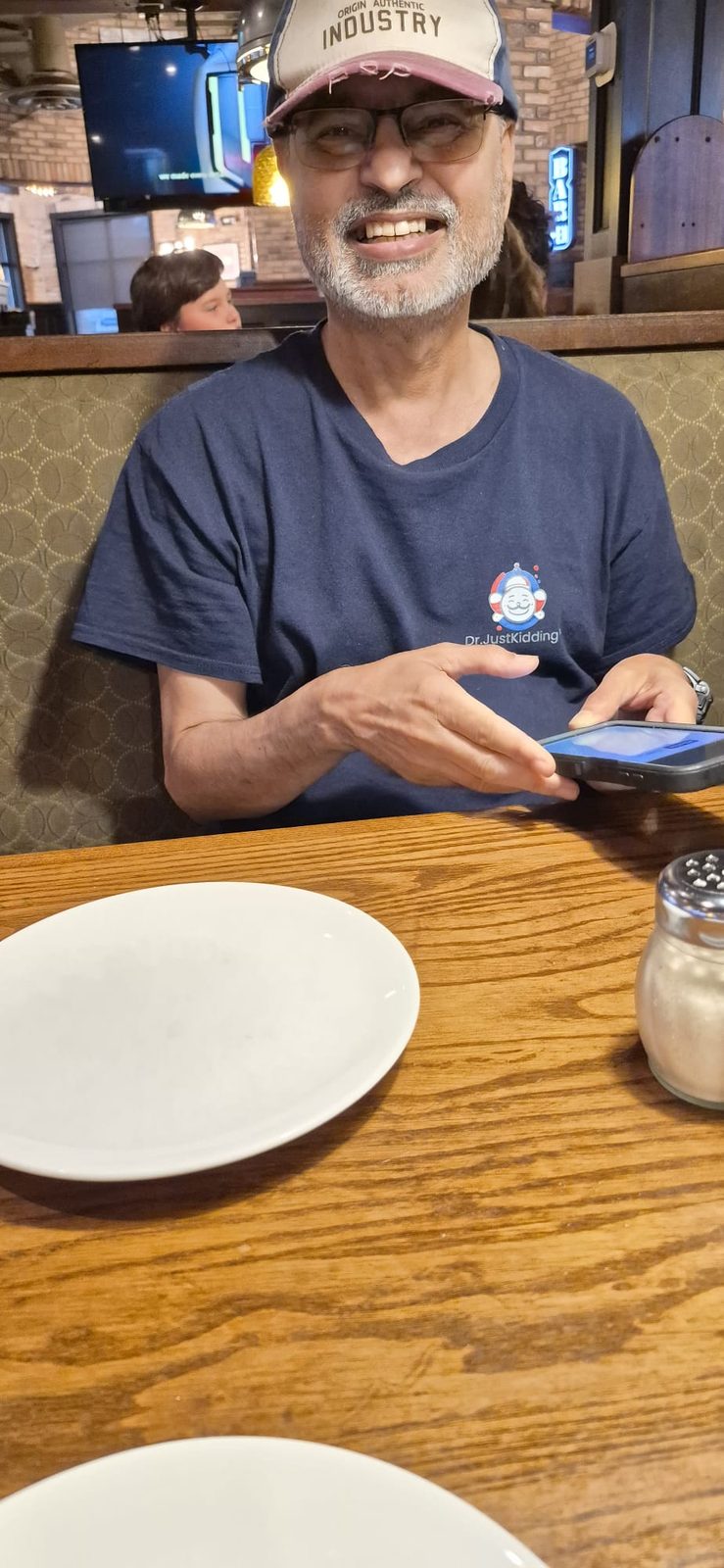 Sridhar Rangaswamy in a navy Dr. JustKidding T-shirt, smiling at a restaurant booth