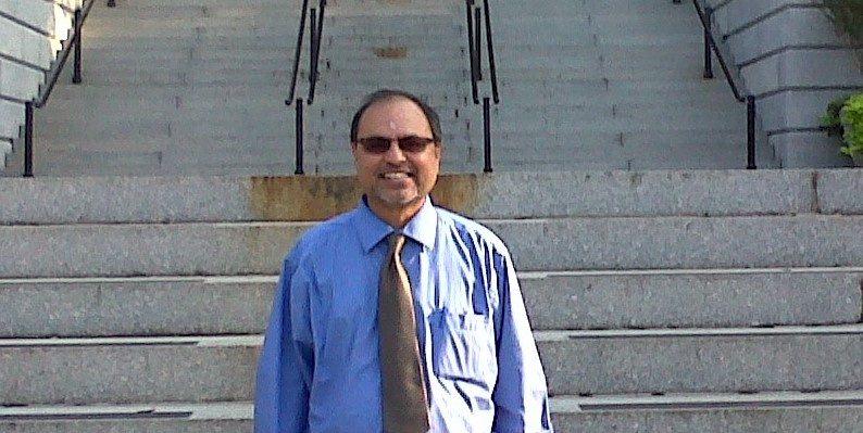 Sridhar Rangaswamy in a blue shirt and tie, smiling on a flight of stone steps