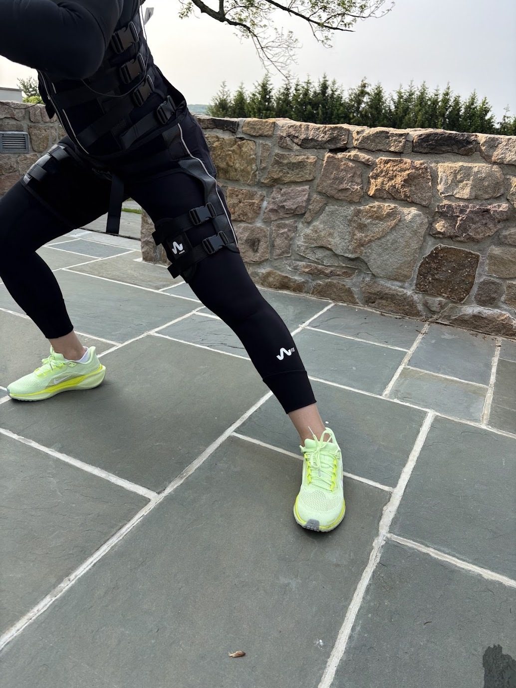 Close-up of an EMS training suit with electrode straps on the thighs during a side lunge on a stone patio