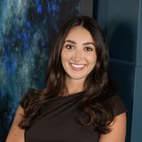 Ariana Stanley, founder and creative director of Creative Concepts Agency, smiling in a brown dress in front of a blue abstract painting