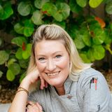 Ashley Ondrick, founder of A (Mostly) Healthy Chef, in a grey chef coat smiling in front of sea grape leaves