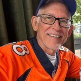 Bret Miller, founder of Sports History Group, smiling in glasses, a blue cap and an orange Denver Broncos jersey