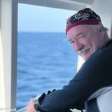 Bruce Campbell, founder of Bruce Campbell Photography, smiling at the rail of a dive boat in a wetsuit and a skull-print bandana