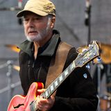 Dan Zalles, singer-songwriter and producer behind Dan Zalles Music, on stage in a khaki cap with a red Gibson semi-hollow guitar