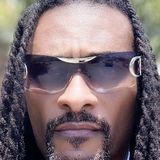 Dearick Milton, founder of Sugar Bee's Boy, LLC, in sunglasses and a white shirt with long locs over his shoulders