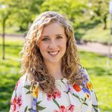 Emma Carpenter, owner of Better Connections Therapy, smiling outdoors in a floral blouse with long curly hair, green trees behind her