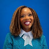 Eunice Adjei, founder of the Jugaad Leadership Program in St. Cloud, Minnesota, smiling in a teal patterned top with a white lace collar against a blue background