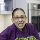 Felicia Dees, founder of Creative Meals by Chef Felicia, in a purple chef coat behind a table of fresh vegetables