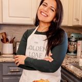 Gaby Miller, owner and baker behind The Golden Loaf Home Bakery, smiling with her arms crossed in her kitchen behind a sliced loaf of sourdough