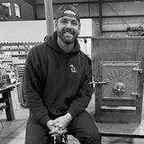 Philip Casteleyn, owner of Nippa Sauna Stoves, smiling in a black hoodie and backwards cap beside a Nippa wood-burning stove