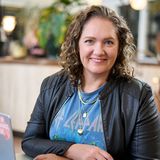 Shannon Gross, founder of Studio One44, smiling at her laptop in a black leather jacket and Def Leppard T-shirt