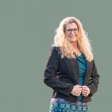 Dr. Tobi Jeurink, founder of Root Function Health, smiling in a black jacket and teal top against a sage green backdrop
