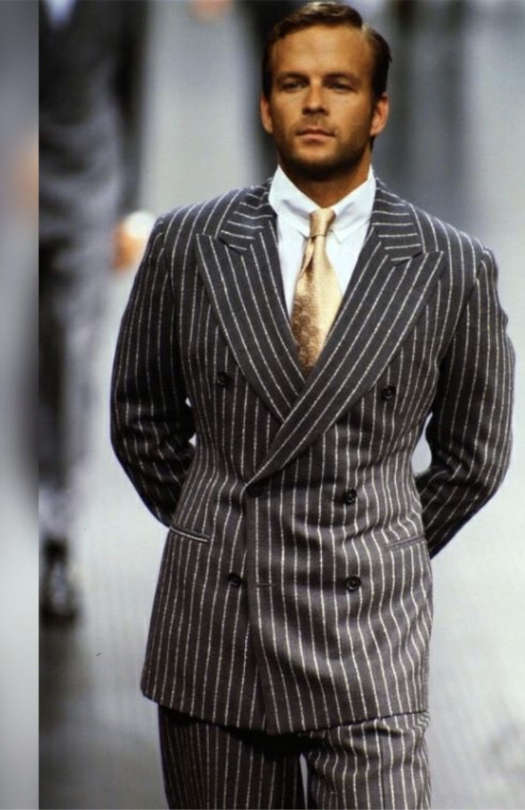 A young William Sanford walking the runway in a grey pinstripe double-breasted suit and gold tie