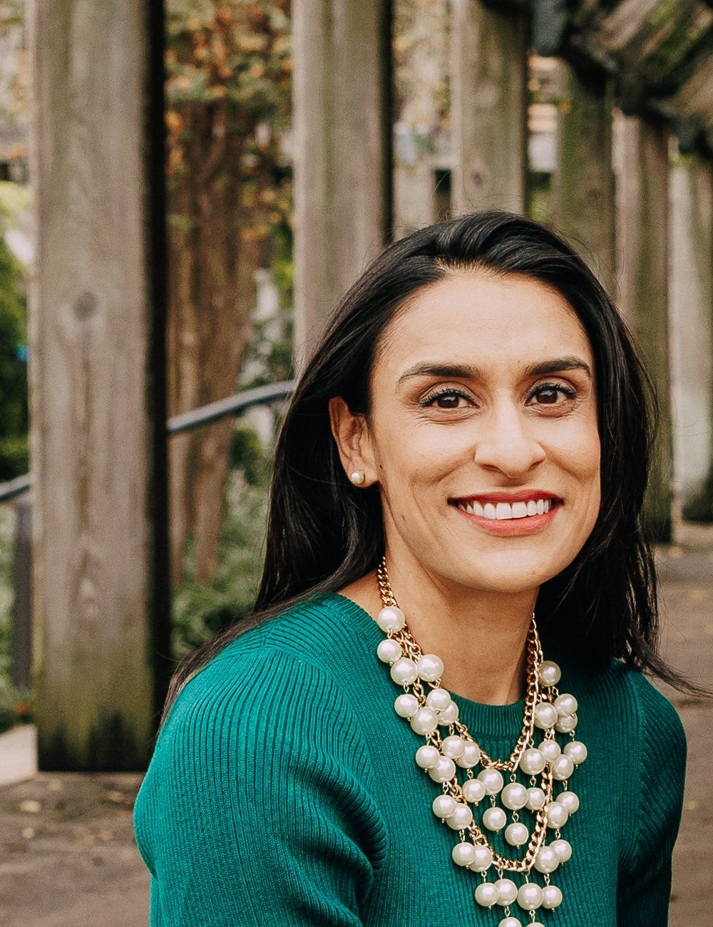 Dr. Zarina Rasheed, board-certified pediatric dentist and owner of Z Pediatric Dentistry, smiling in a green dress and pearl necklace