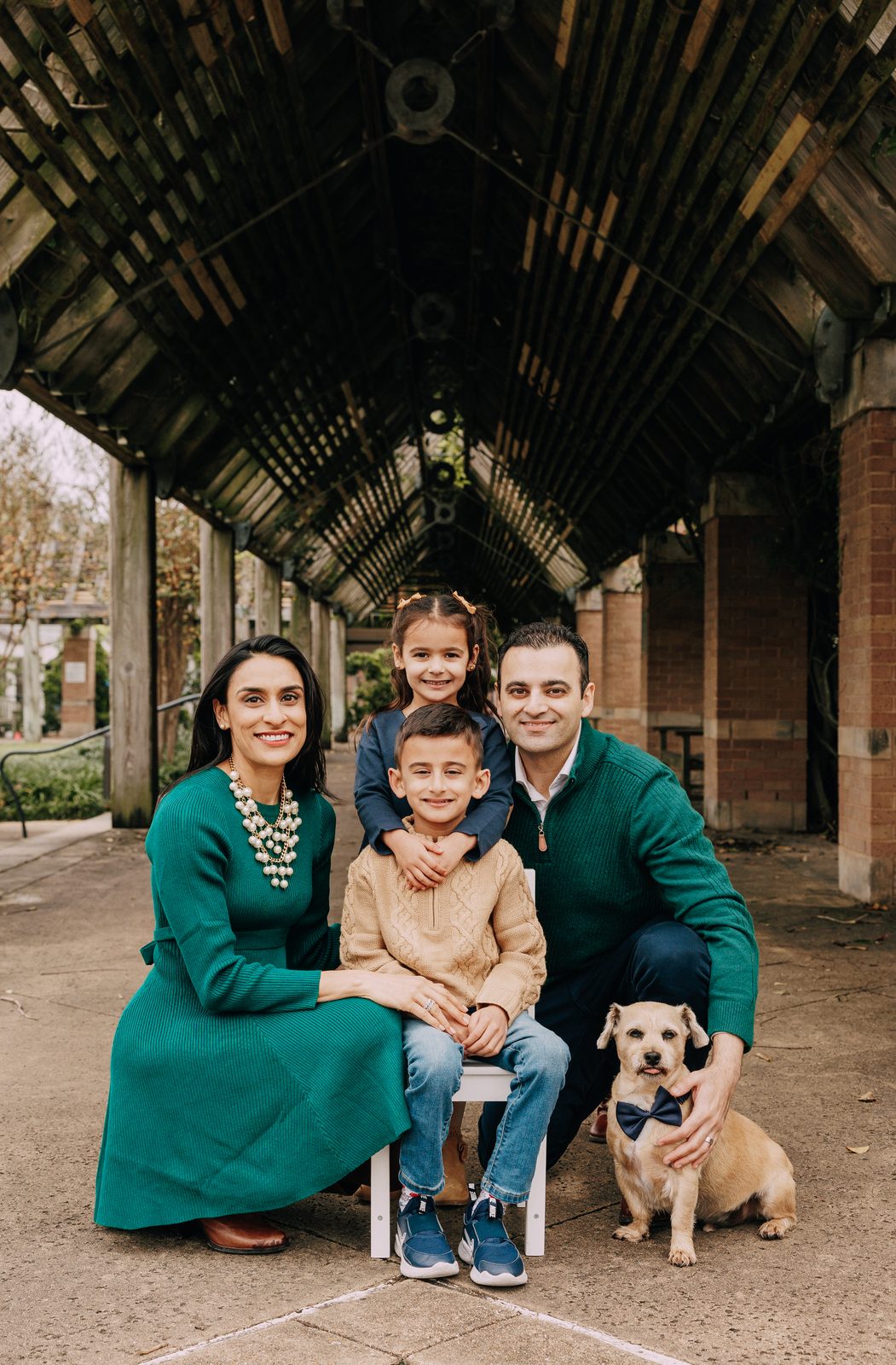 Dr. Zarina Rasheed with her husband, her two children and the family dog under a wooden pergola in Houston