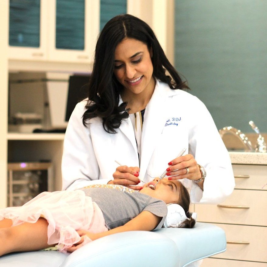 Dr. Zarina Rasheed in a white coat examining a young patient in the dental chair at Z Pediatric Dentistry