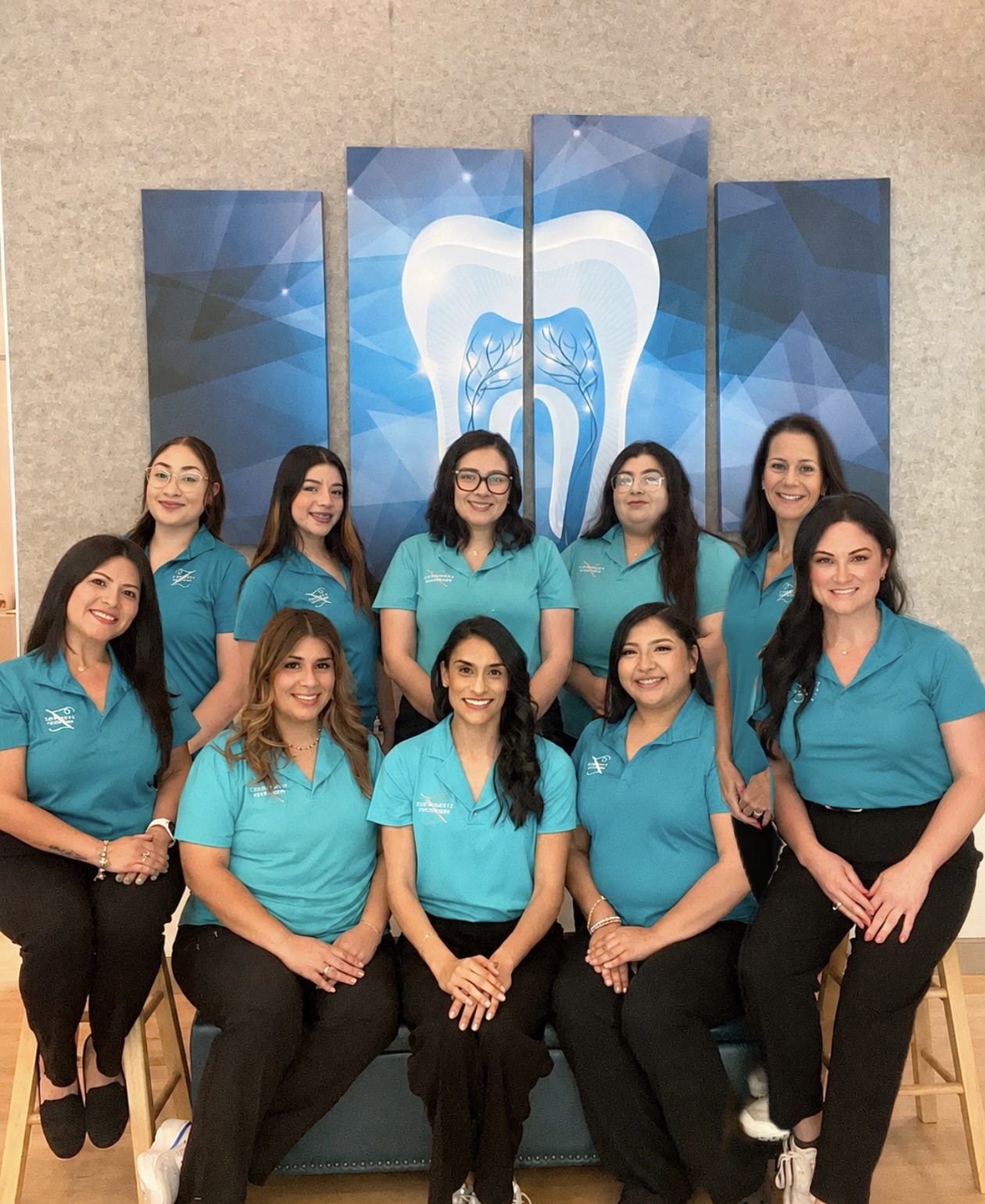 The Z Pediatric Dentistry team in teal polo shirts in front of a blue tooth mural